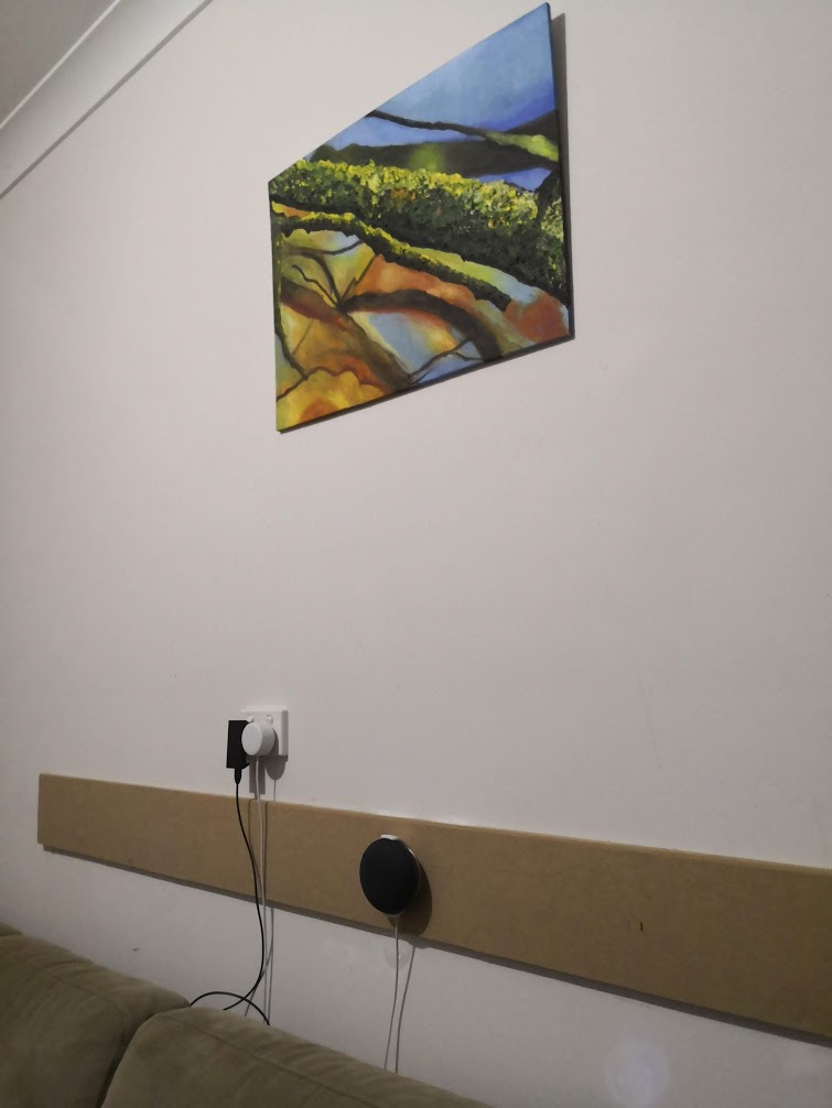 A small Google Home device attached to a wall under a piece of art